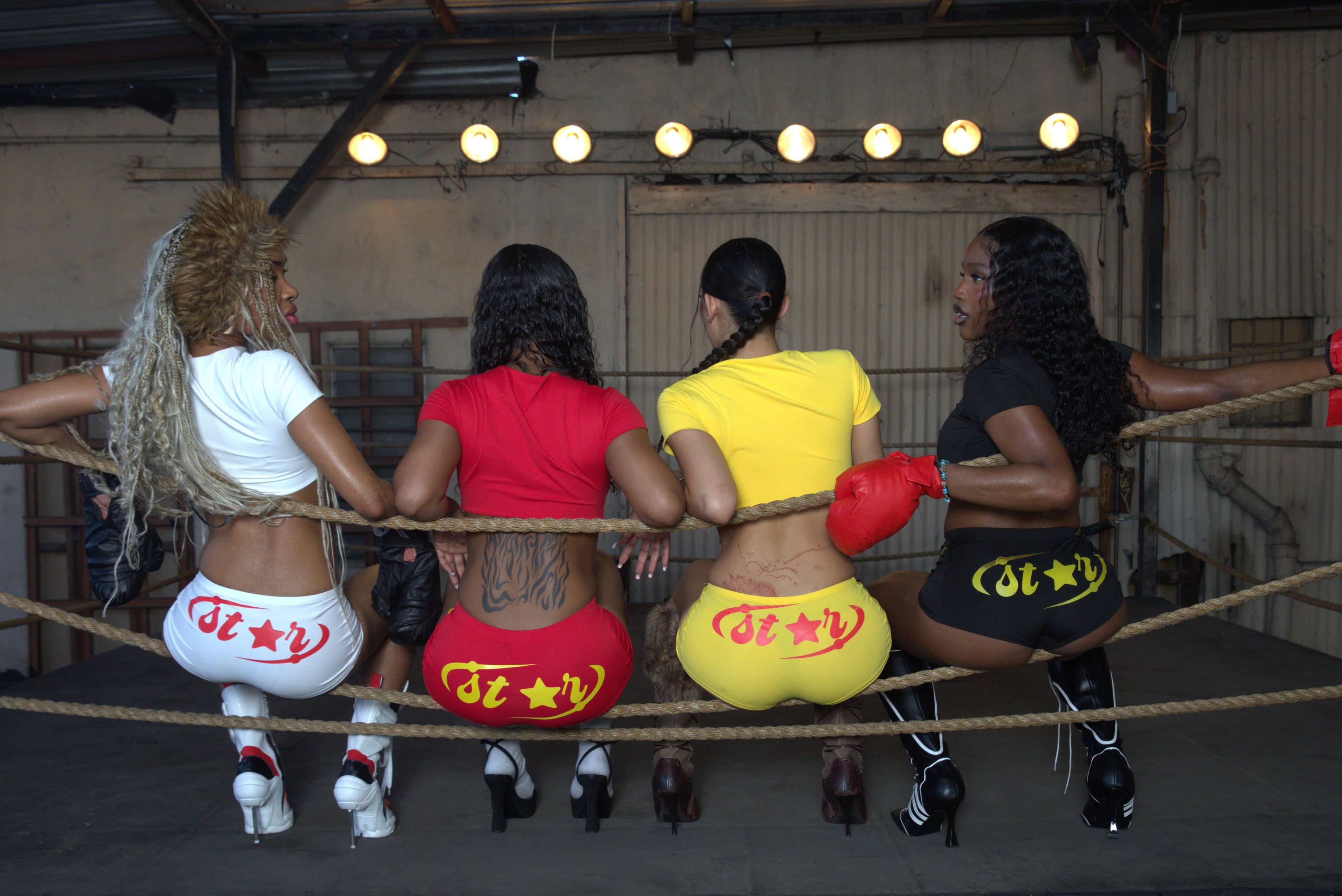 Four women in colorful outfits standing in a boxing ring.